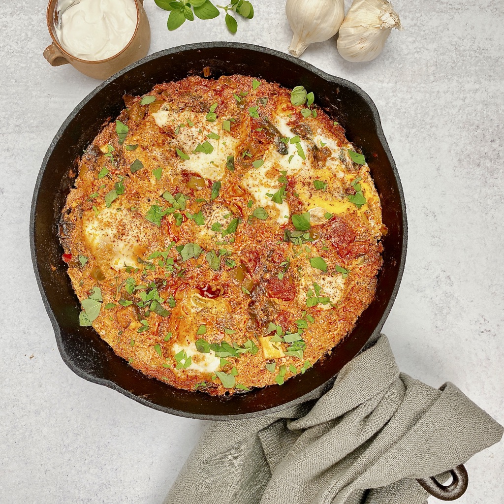 image of cast iron pan with shakshuka eggs poached in tomato and seasonings sauce