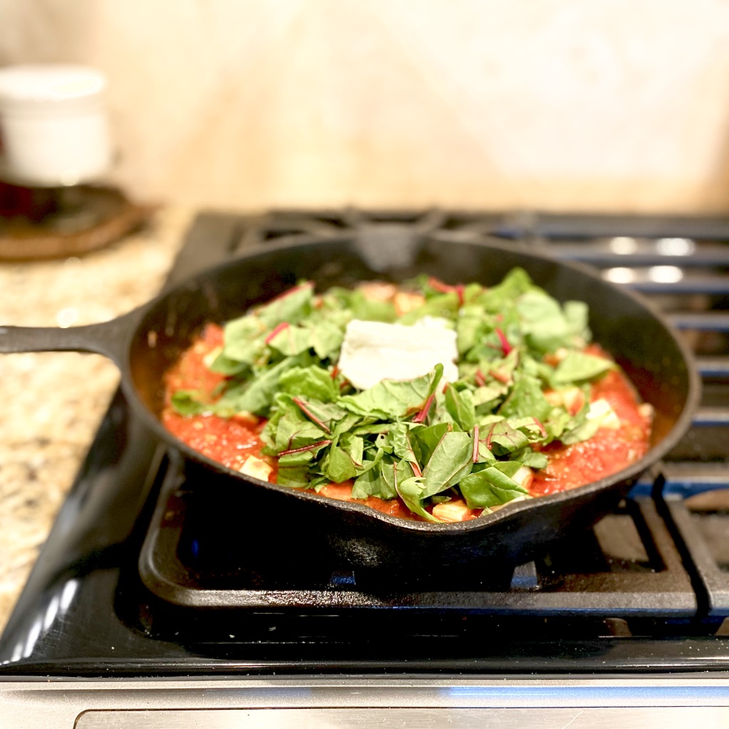 image of cast iron pan cooking shakshuka on the stovetop